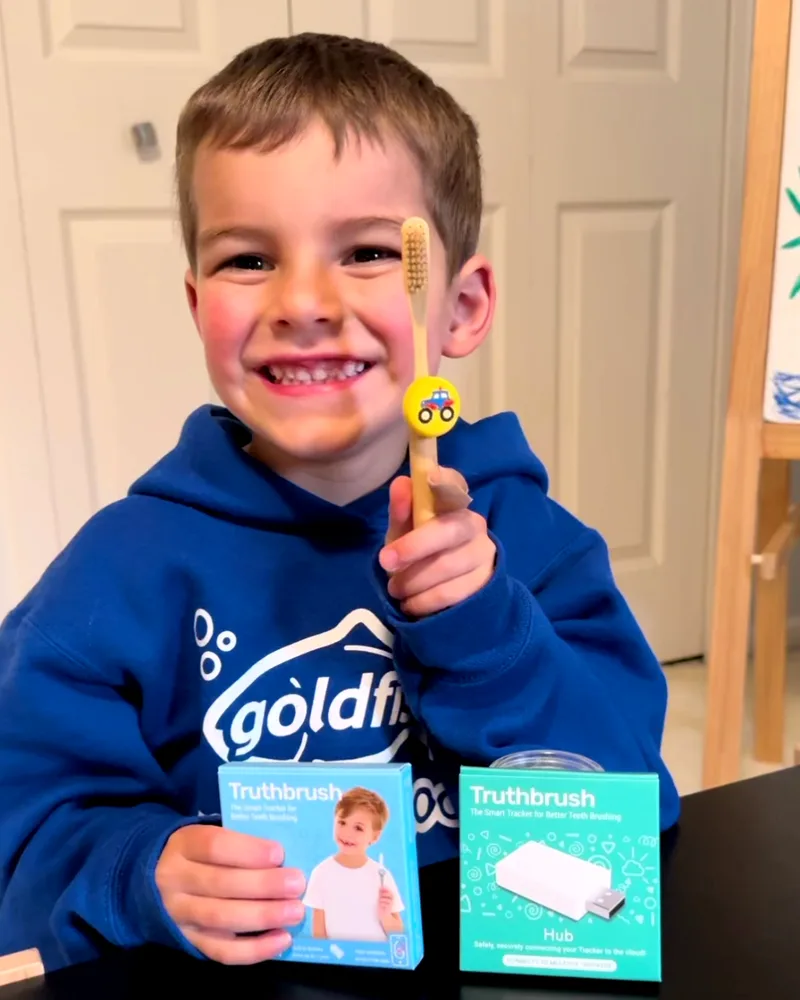 Boy with a truck-skin Truthbrush Tracker on his toothbrush, with Classic Tracker and Hub boxes