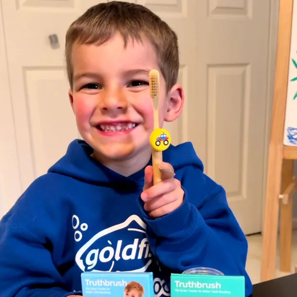 Boy with a truck-skin Truthbrush Tracker on his toothbrush, with Classic Tracker and Hub boxes
