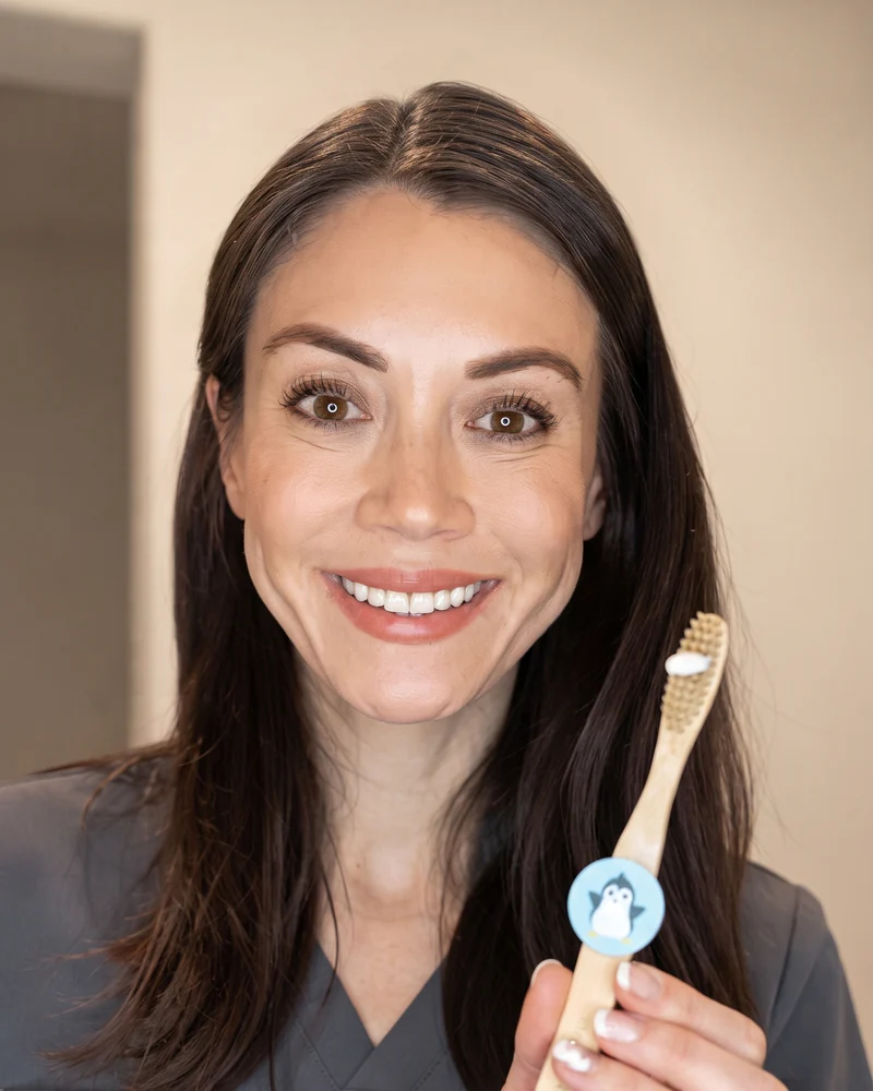 Adult holding a bamboo toothbrush with a penguin-skin Truthbrush Tracker