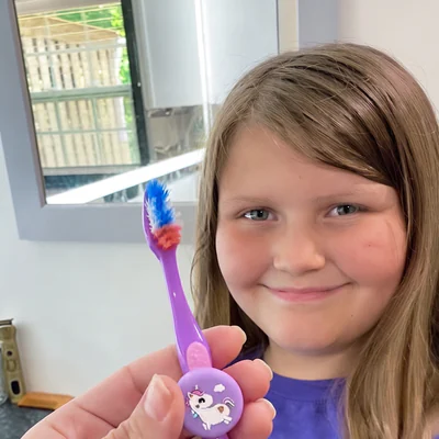 Girl smiling beside a toothbrush fitted with a unicorn-skin Truthbrush Tracker