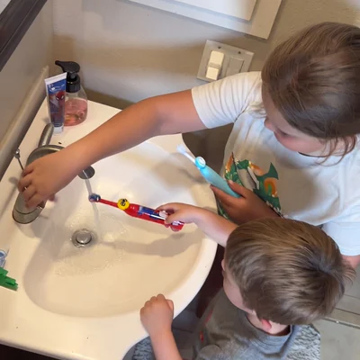 Two siblings at the bathroom sink rinsing a toothbrush fitted with a Truthbrush Tracker